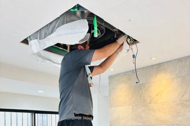 天井に埋め込まれた業務用エアコンを分解し、クリーニングしている作業員の様子