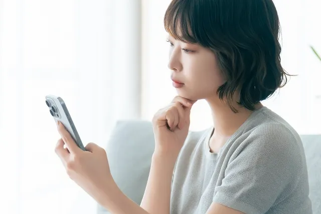 真剣な表情で、スマートフォンの画面を見つめている若い女性