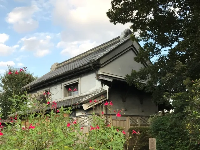 志木市にある村山快哉堂。赤い花が咲く庭に囲まれた白壁と瓦屋根の伝統的な蔵造りの建物